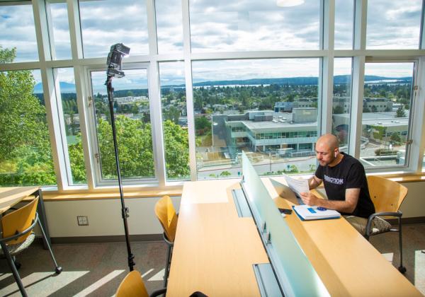 A man working at a table overlooking a view of the city. 