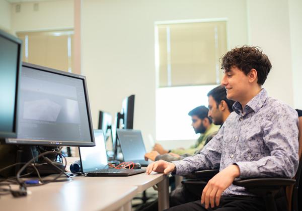 Young man at a computer workstation in a classroom.